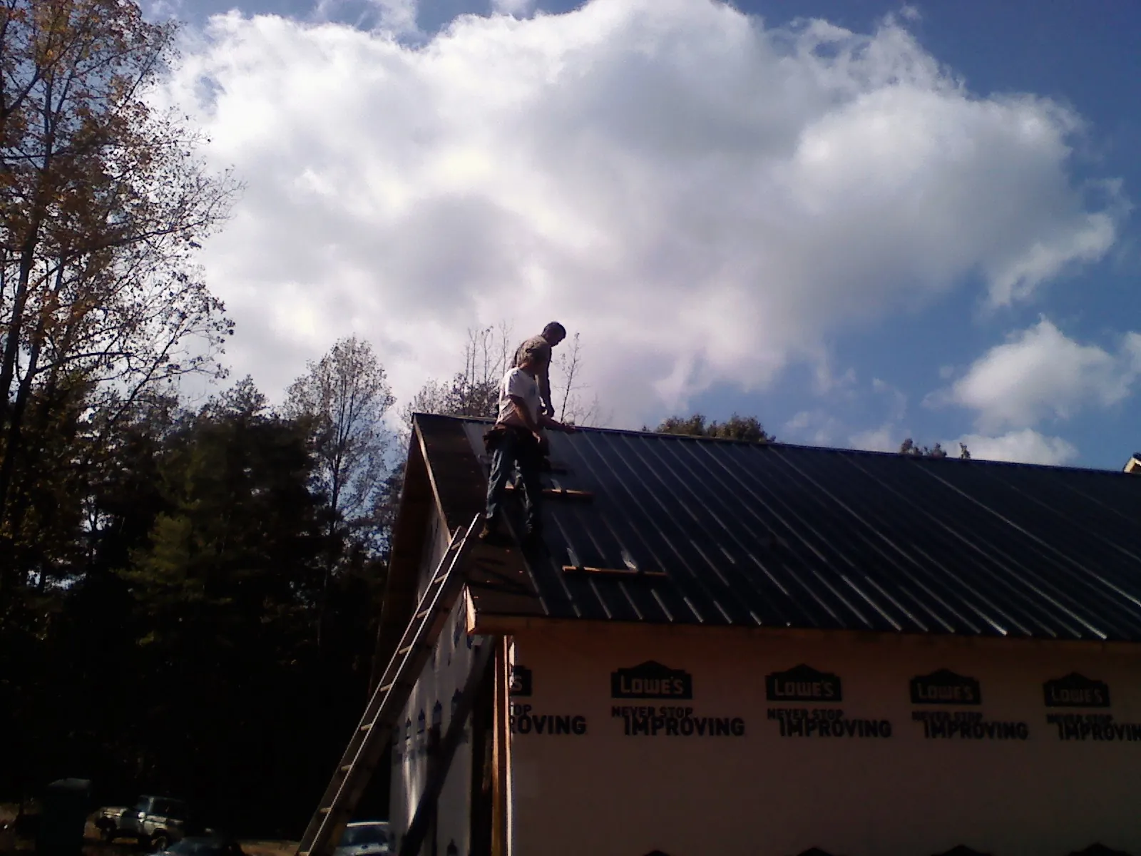 Roofer fastening dark metal panels high against a cloudy sky, from a Roof Inspection job in Boring